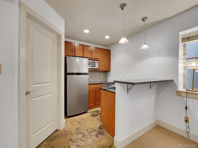 kitchen with freestanding refrigerator, decorative backsplash, brown cabinets, and dark countertops
