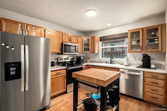 kitchen with a sink, light wood-style flooring, appliances with stainless steel finishes, and glass insert cabinets