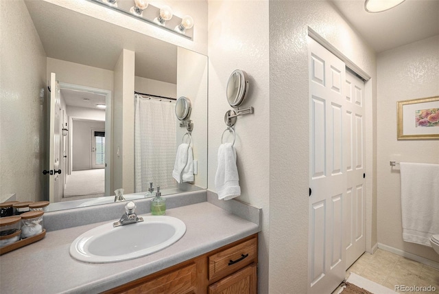 full bathroom featuring toilet, a textured wall, and vanity