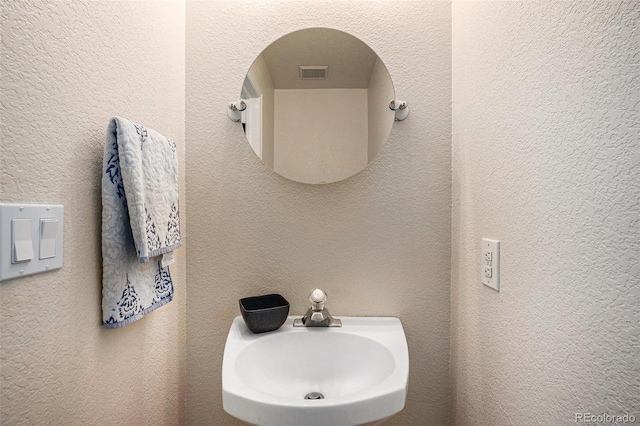 bathroom with visible vents, a sink, and a textured wall
