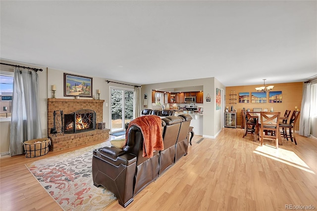 living area featuring a chandelier, a fireplace, light wood-style flooring, and baseboards