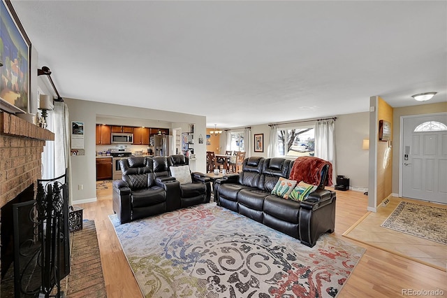 living room with a brick fireplace, light wood-style flooring, and baseboards