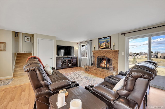 living room featuring a fireplace, light wood finished floors, visible vents, baseboards, and stairs