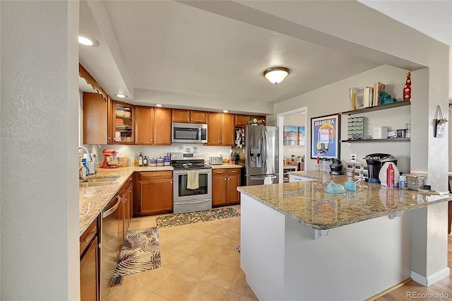 kitchen with a peninsula, appliances with stainless steel finishes, brown cabinetry, and a sink