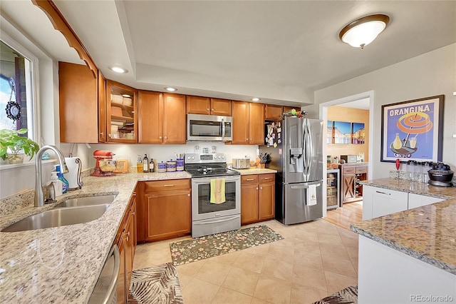 kitchen featuring light stone countertops, appliances with stainless steel finishes, brown cabinets, and a sink