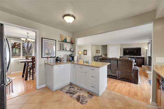 kitchen featuring light stone counters, a notable chandelier, light tile patterned floors, freestanding refrigerator, and a peninsula