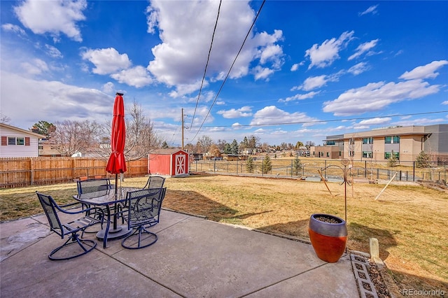 view of patio with outdoor dining space, a storage unit, a fenced backyard, and an outbuilding