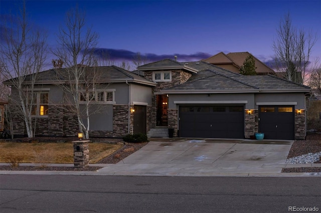 prairie-style home with stucco siding, stone siding, a garage, and driveway