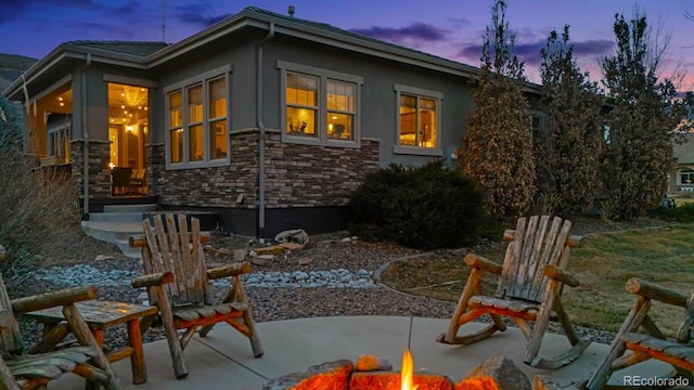 back of house at dusk featuring a patio area, stone siding, stucco siding, and an outdoor fire pit