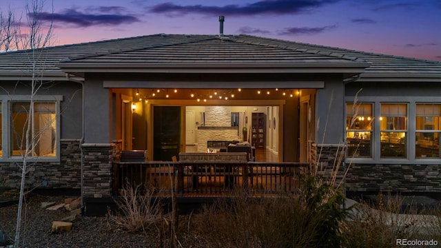 back of house at dusk with a tile roof and stone siding