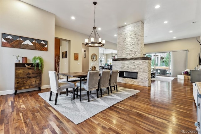 dining space featuring recessed lighting, a notable chandelier, a stone fireplace, and wood finished floors