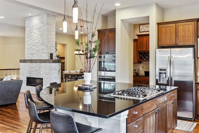 kitchen featuring a kitchen island, tasteful backsplash, wood finished floors, appliances with stainless steel finishes, and a fireplace