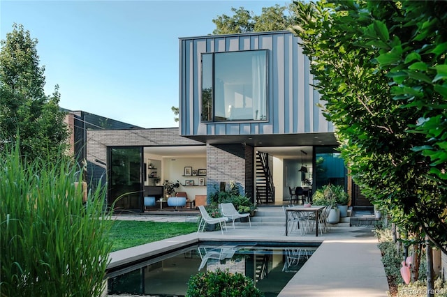 rear view of property featuring an outdoor pool, stairway, a patio area, and brick siding