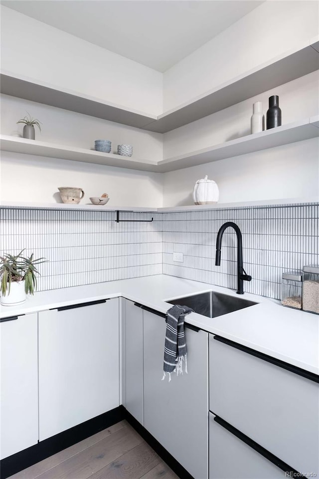 kitchen featuring tasteful backsplash, open shelves, light countertops, dark wood-style floors, and a sink