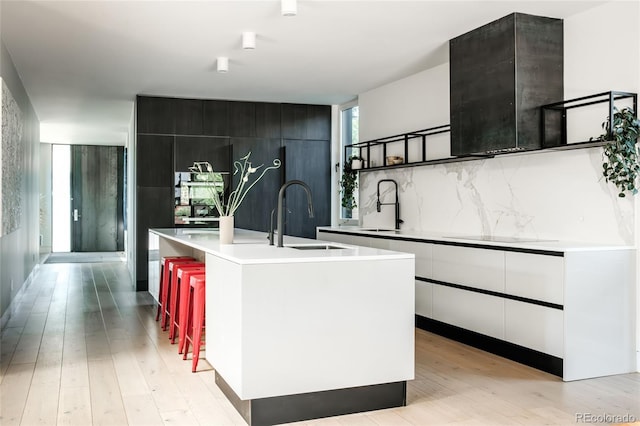 kitchen featuring light wood finished floors, a center island with sink, modern cabinets, and a sink