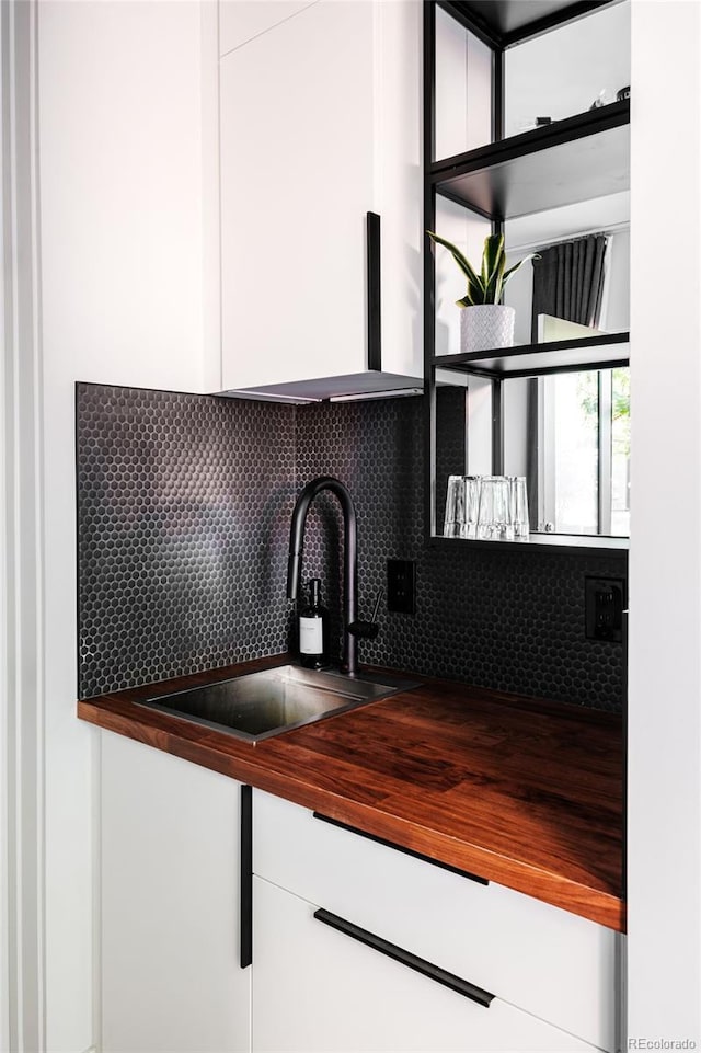 kitchen featuring a sink, decorative backsplash, butcher block countertops, and white cabinetry