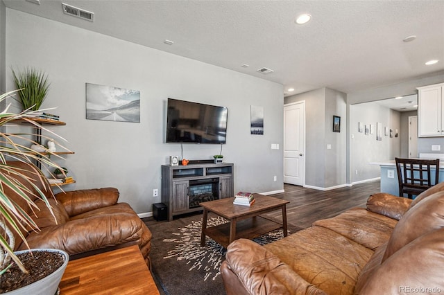 living area with dark wood-style flooring, a fireplace, recessed lighting, visible vents, and baseboards