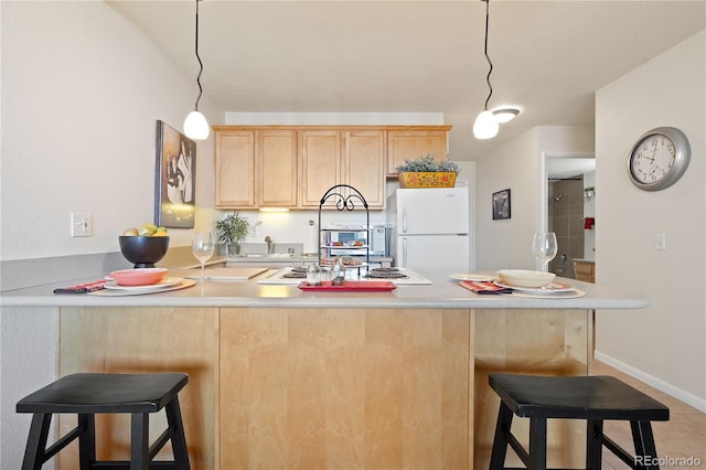 kitchen with a breakfast bar area, a peninsula, freestanding refrigerator, light brown cabinetry, and light countertops