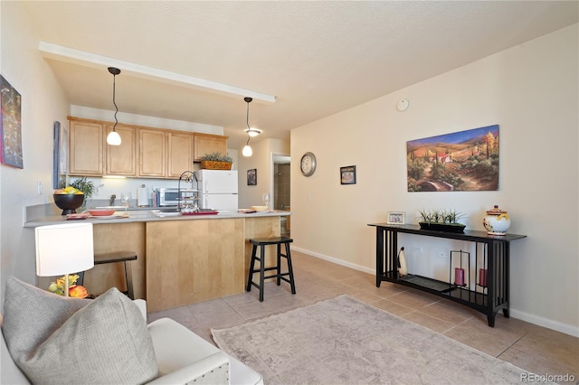 kitchen featuring light brown cabinetry, a peninsula, a kitchen breakfast bar, freestanding refrigerator, and light tile patterned flooring