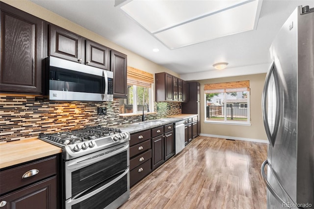 429 Arrowhead Dr, Loveland, CO 80537 - kitchen featuring stainless steel appliances, dark brown cabinetry, decorative backsplash, a sink, and light wood-type flooring