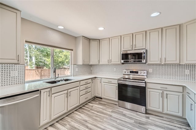 kitchen with sink, light wood-type flooring, decorative backsplash, and appliances with stainless steel finishes