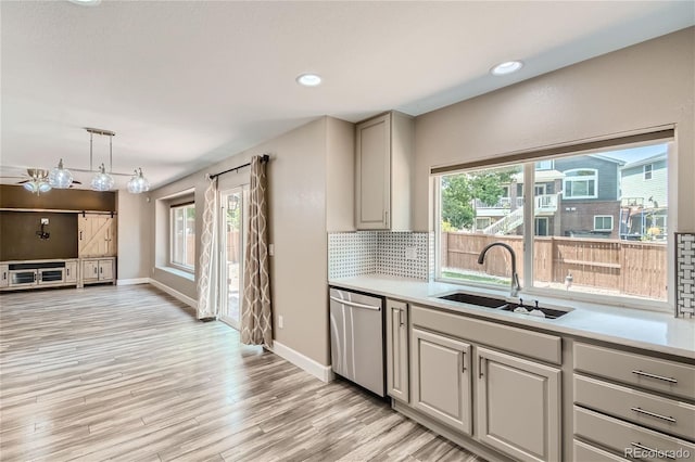 kitchen featuring stainless steel dishwasher, sink, decorative light fixtures, backsplash, and light hardwood / wood-style floors