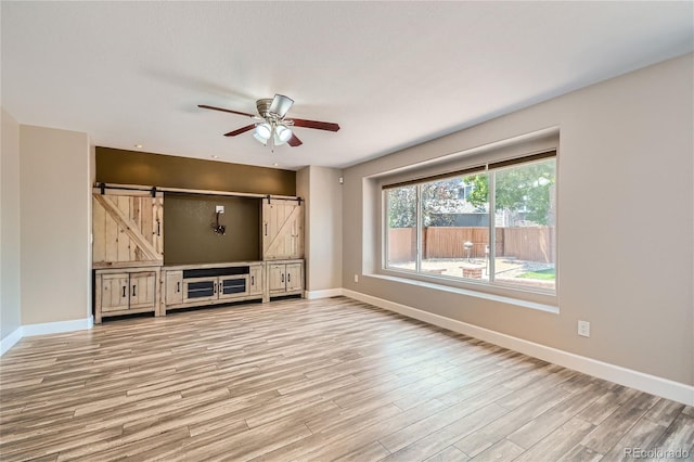 unfurnished living room with light hardwood / wood-style floors, ceiling fan, and a barn door