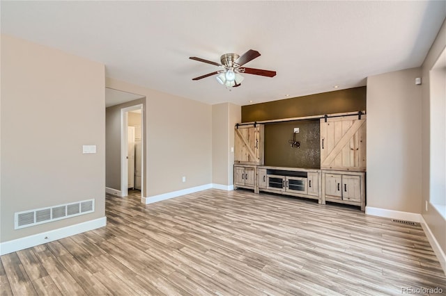 unfurnished living room featuring light wood-type flooring, ceiling fan, and a barn door