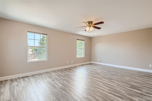 spare room with light wood-type flooring, ceiling fan, and a healthy amount of sunlight