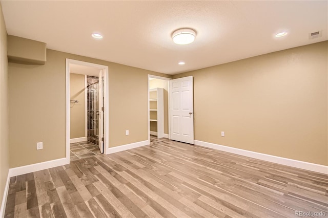 unfurnished bedroom with ensuite bath, wood-type flooring, a closet, and a walk in closet