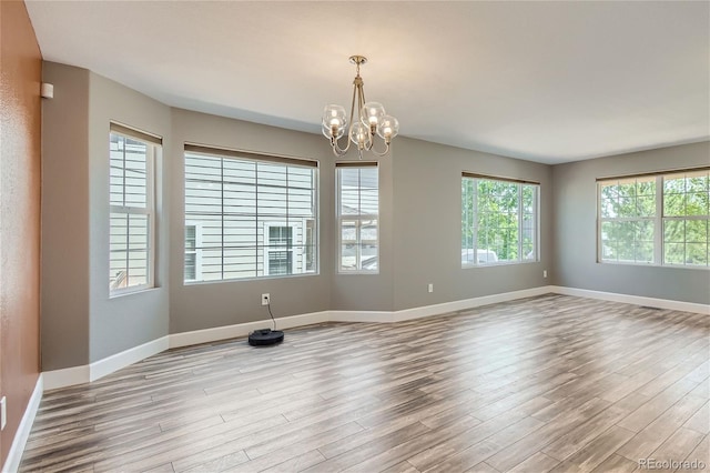 empty room with plenty of natural light, a chandelier, and light wood-type flooring