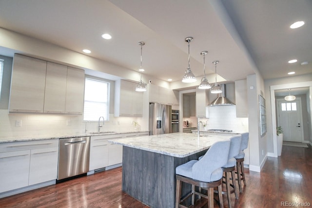 kitchen with wall chimney range hood, appliances with stainless steel finishes, a sink, recessed lighting, and backsplash