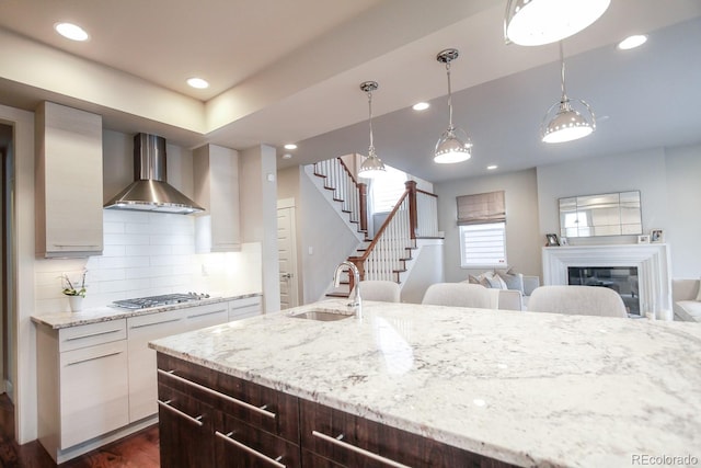kitchen with a sink, stainless steel gas cooktop, wall chimney exhaust hood, recessed lighting, and backsplash