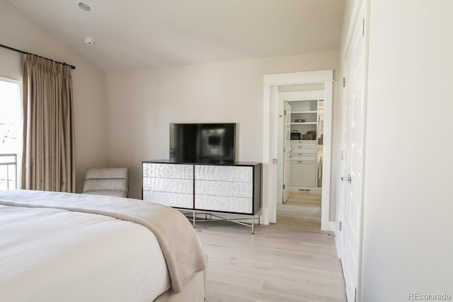bedroom with light wood-style floors, vaulted ceiling, and fridge