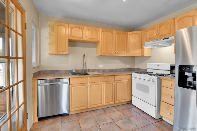 kitchen with light brown cabinetry, tile countertops, under cabinet range hood, a sink, and appliances with stainless steel finishes