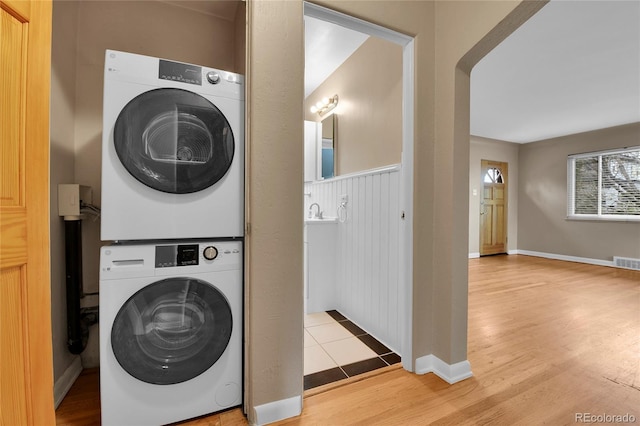 laundry room with stacked washer / drying machine, visible vents, wood finished floors, and laundry area