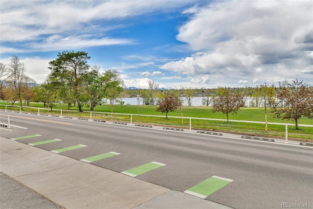 view of street with sidewalks, a water view, and curbs