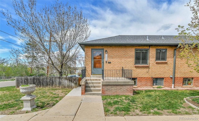 view of front facade with fence, brick siding, roof with shingles, and a front yard