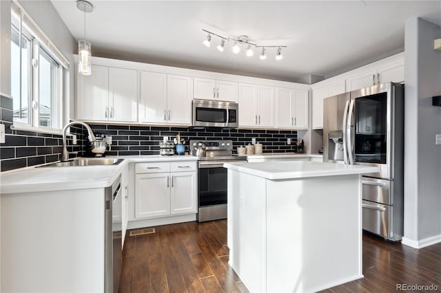 kitchen featuring a center island, sink, white cabinetry, hanging light fixtures, and stainless steel appliances