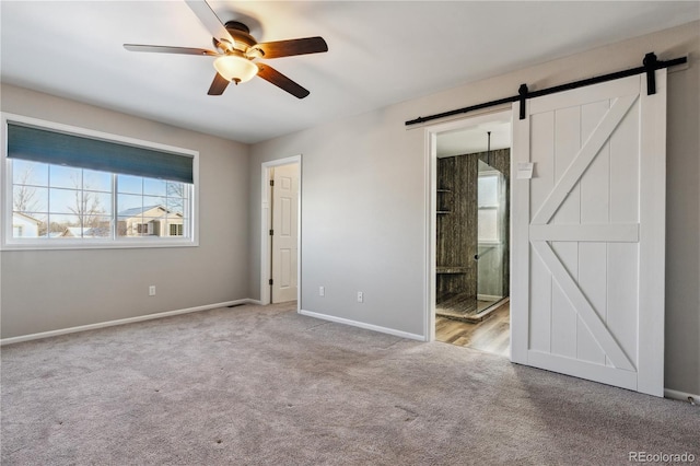 unfurnished bedroom with ceiling fan, a barn door, light carpet, and connected bathroom