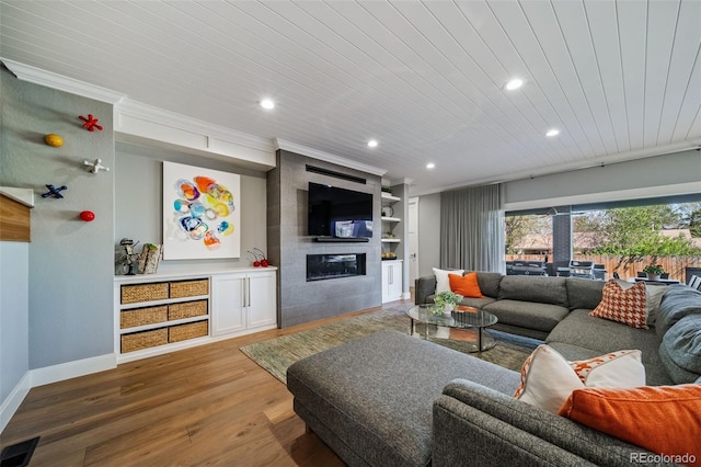 living area with a large fireplace, recessed lighting, baseboards, wood finished floors, and ornamental molding