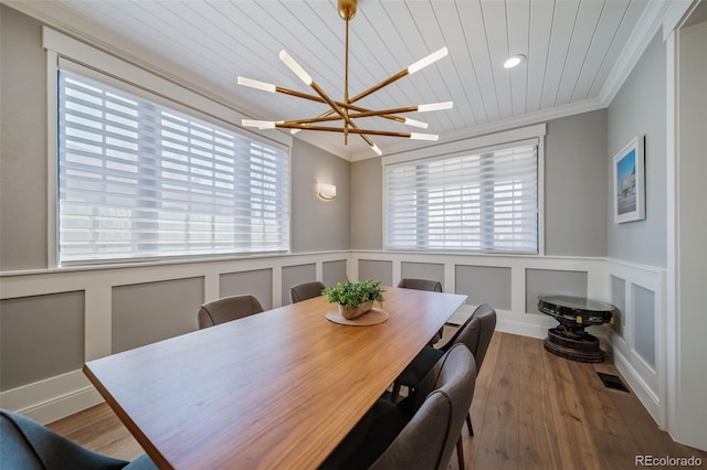 dining area with crown molding, wainscoting, wood finished floors, and a notable chandelier