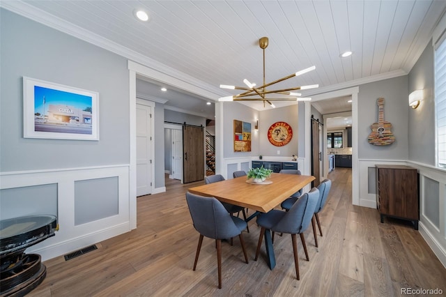 dining room with a barn door, wood ceiling, a wainscoted wall, and ornamental molding
