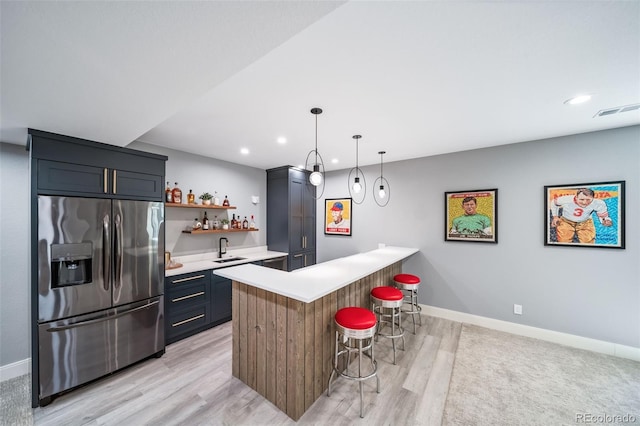 kitchen with a peninsula, a kitchen bar, stainless steel refrigerator with ice dispenser, light countertops, and a sink
