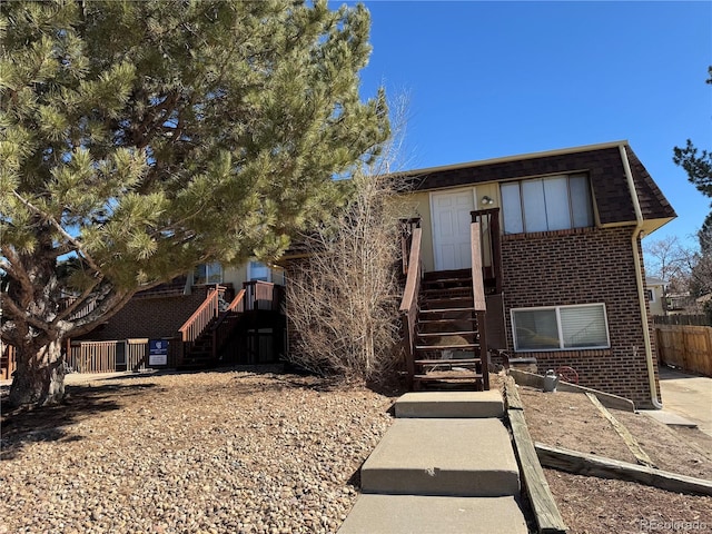 view of front of home featuring stairs, fence, and brick siding