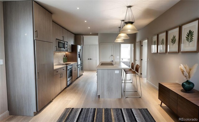 1643 Boulder St Unit 211, Denver, CO 80211 - kitchen with stainless steel appliances, a kitchen island with sink, a sink, light wood-type flooring, and light countertops