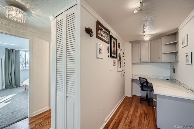 office space with crown molding, a textured ceiling, built in desk, and wood finished floors