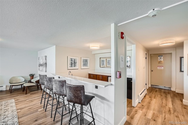 kitchen featuring a kitchen bar, light wood-type flooring, light countertops, and baseboard heating