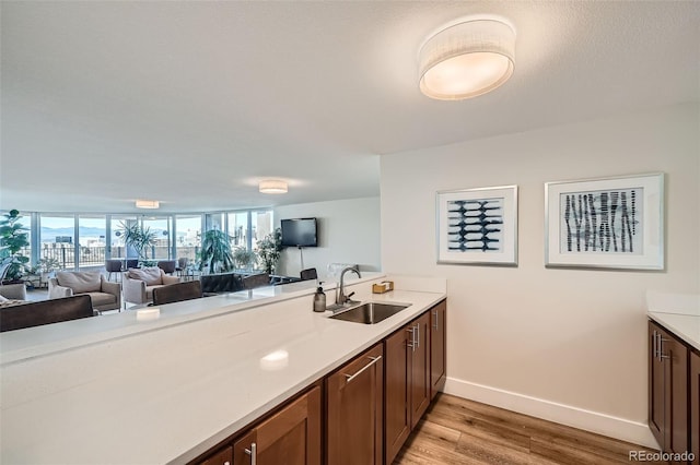 kitchen with baseboards, a peninsula, light countertops, light wood-type flooring, and a sink