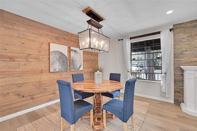 dining area featuring visible vents, baseboards, light wood-style flooring, wood walls, and a notable chandelier